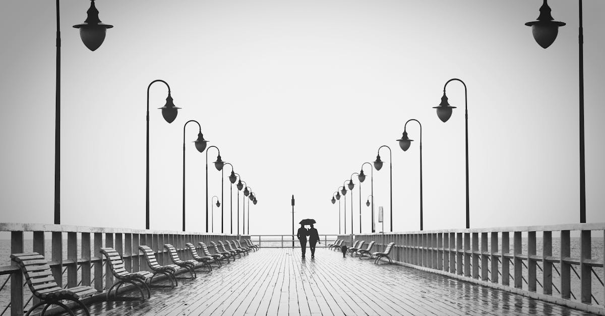 A couple holding umbrellas walks on a rainy boardwalk, embodying romance and tranquility.